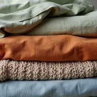 Empilement de textiles naturels scandinaves — lin vert sauge, coton terracotta et laine tricotée beige